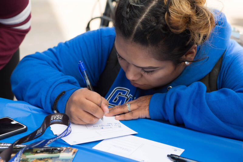  Female student kneeling while writing on a postcard