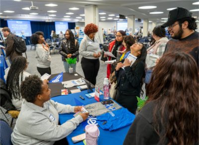 people crowded around table with blue tablecloth, woman in center throwing head back to laugh