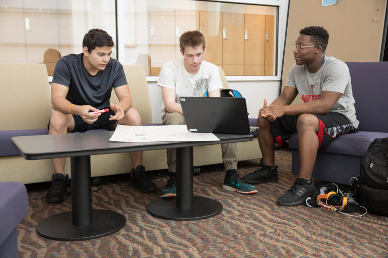 three young men talking in chairs, before computer