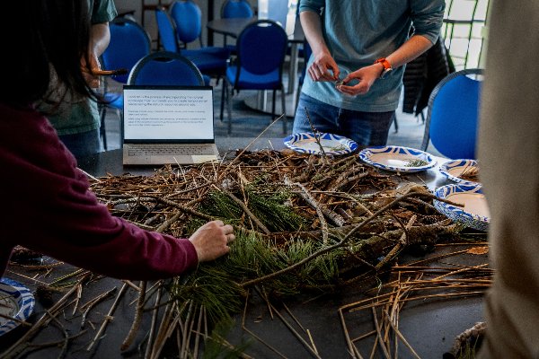 Two people assemble twigs and pine needles into a circular abstract land sculpture. 