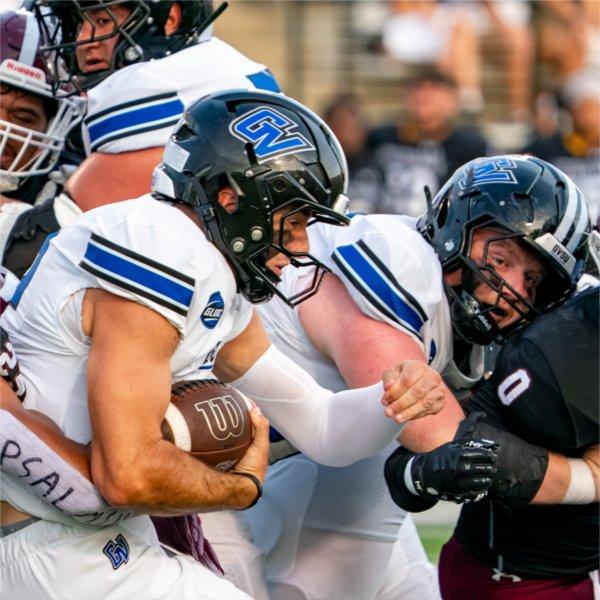 A Grand Valley football player carries the football while a teammate blocks for him,