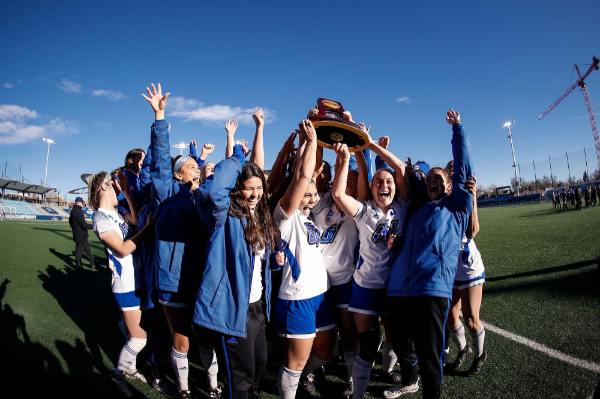Soccer players lift trophy over their heads in celebration.