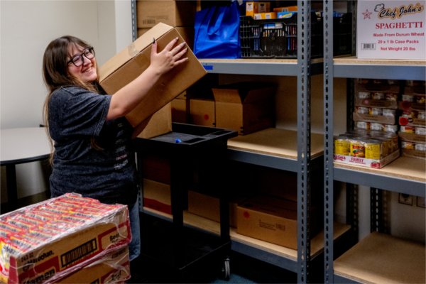 A woman lifts a cardboard box onto a storage shelf full of other boxes. 
