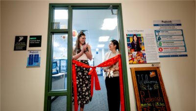 Mimi Sperl and Susana Villagomez stand in the doorway of Replenish behind a red ribbon tied in a bow. 