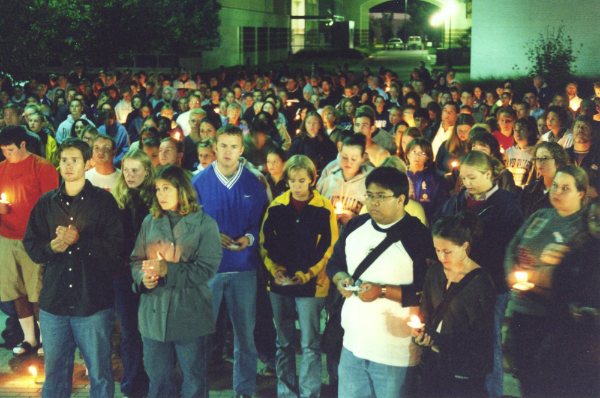 A large gathering of people hold candles at night.