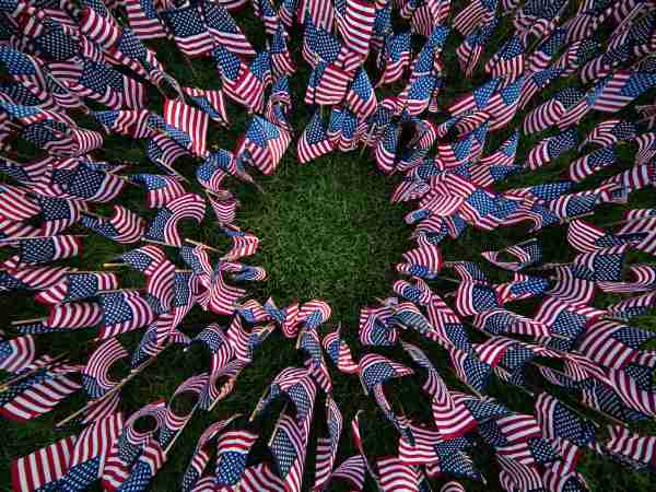 Many small American flags are placed in the grass in the shape of a circle.