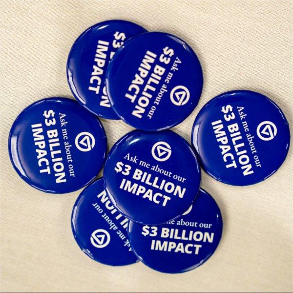 This image shows a collection of blue buttons arranged on a light-colored surface. Each button features the text:  �Ask me about our $3 BILLION IMPACT�