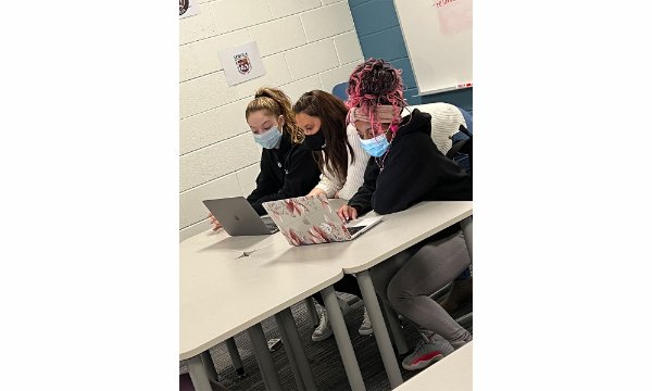 two high school students and a GVSU TRIO advisor are seated looking at two laptop computers