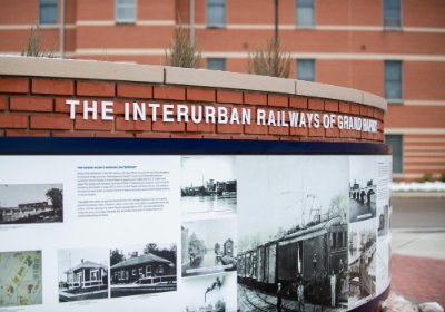 An art exhibit showing through photos and information. It is placed on a brick wall under the words The Interurban Railways of Grand Rapids