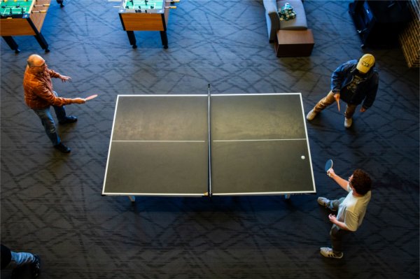 An overhead view of three people playing table tennis indoors.