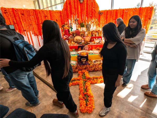 Students file by a Day of the Dead altar that is bright orange. 