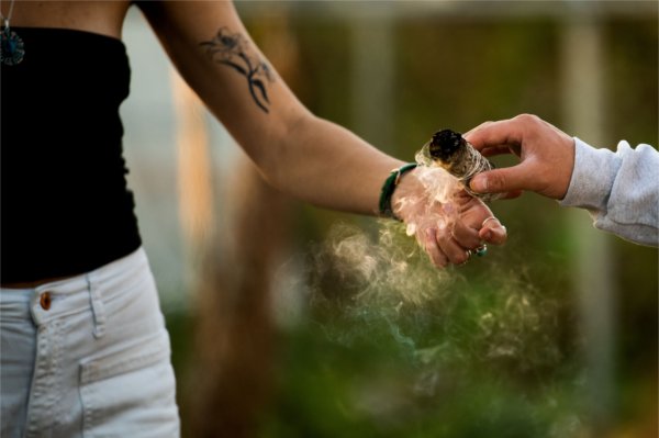 A detail of two hands passing a smoking smudge stick.