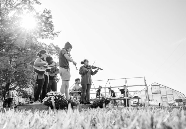 A group of college students play music outdoors under the sunlight. 