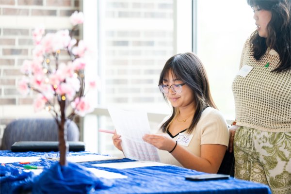 A college student smiles while looking at a piece of paper. 