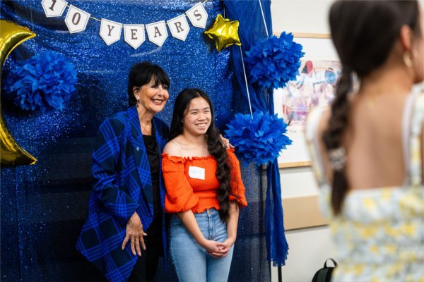 A university president smiles while posing with a student wearing orange. 