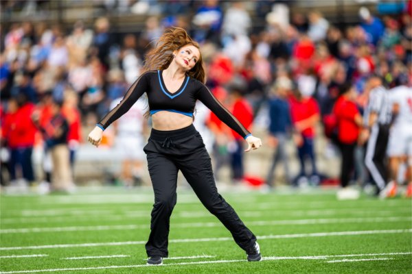 A college dance team member flicks her hair while performing on a football field. 