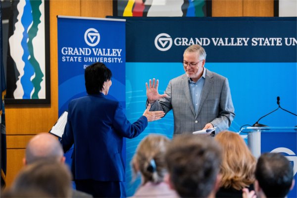 A university president and business person high five as they pass each other to speak at an event. 