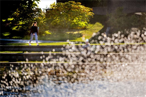 A student walks past the Zumberge Pond fountain during a sunny fall day on a college campus. 