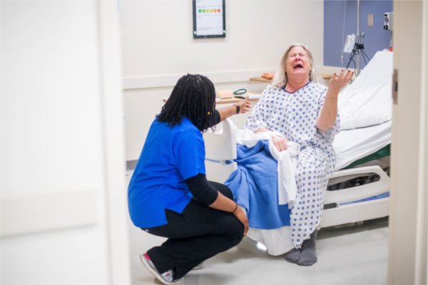 KCON student Amarachi Oboh kneels in front of 'Janet,' a standardized patient, during a pilot simulation in the hospital suite of the Simulation Center in the DeVos Center for Interprofessional Health.
