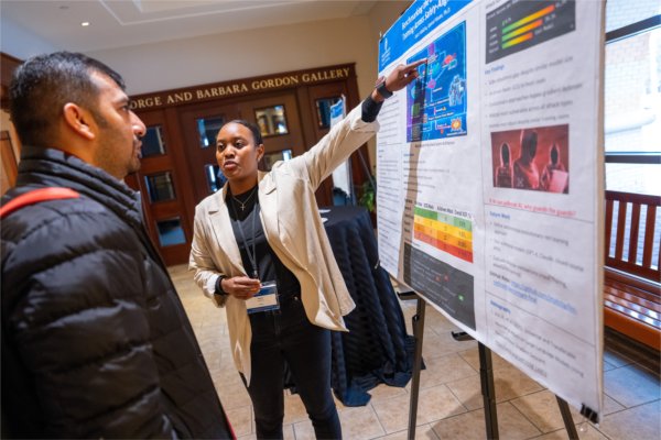 A person points to a poster with lots of graphics and other information while talking to another person.