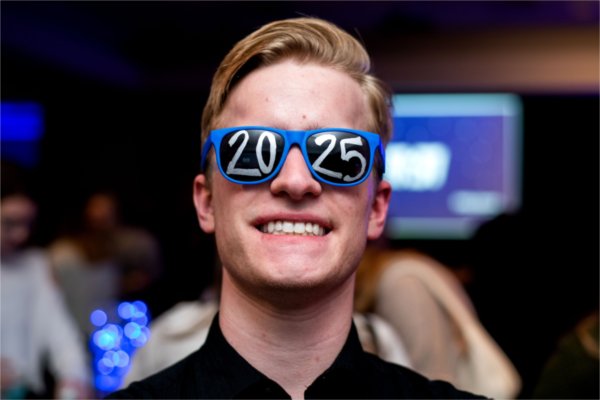 A person smiles while wearing sunglasses with "20" on one side and "25" on the other.