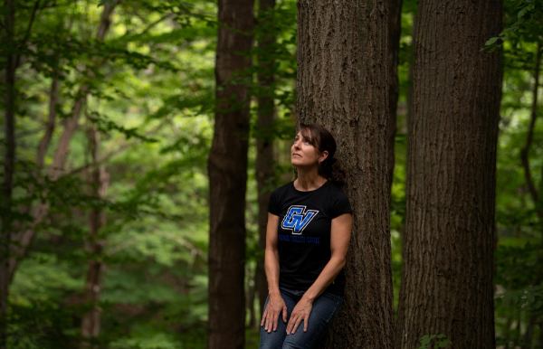 A person wearing a "GV" shirt leans against a tree and looks upward.