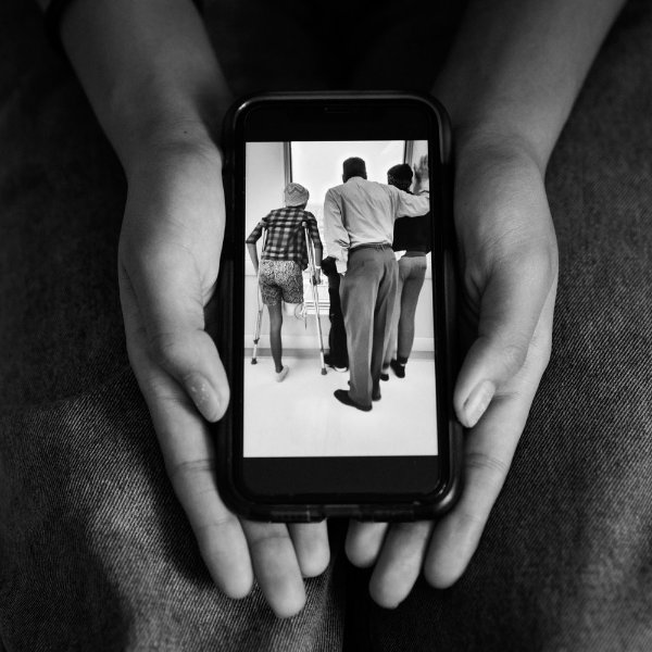 pair of hands holding a smartphone, showing a photo of a teen girl on crutches learning to walk after an amputation. Two other people look on in the photo.