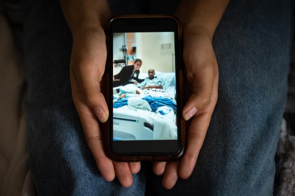 pair of hands holding a smartphone, showing a photo of a nurse hugging a girl in a hospital bed. The girl is bald after chemotherapy.