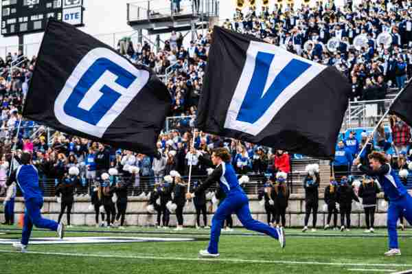 Cheerleaders run onto football field with flags