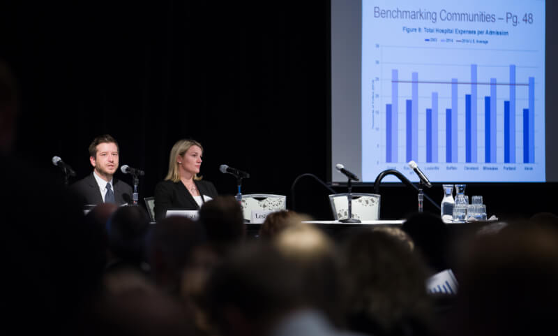 2 people at table, powerpoint slide in background