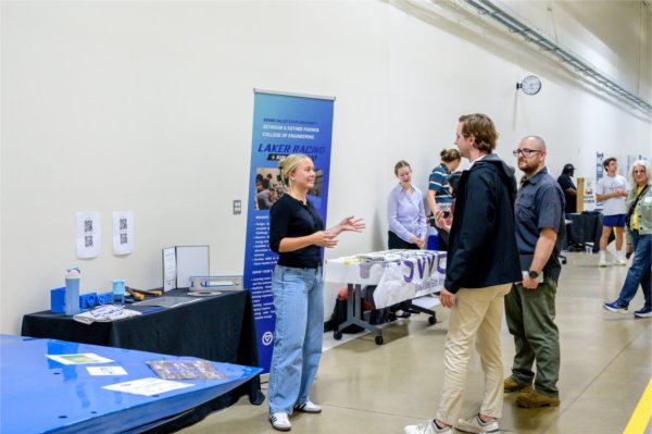 two people chat with a student in a hallway during a reception in front of the Laker Racing car