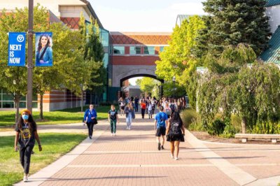 students walking on Allendale Campus; banner hanging from lightpost reads Next is Now