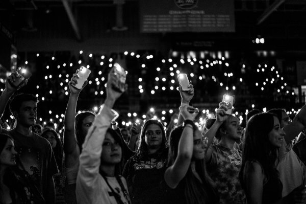  In a large dark room, students hold up their cell phones with the flash lights on to illuminate the dark. 