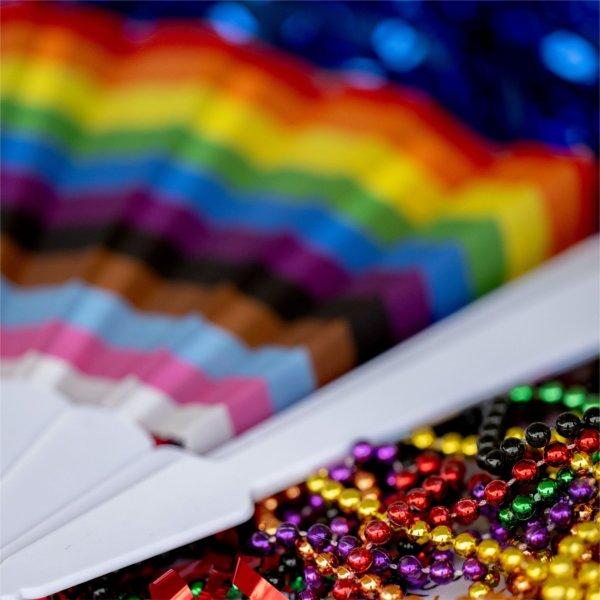 A pride flag fan sits on top of a pile of rainbow beaded necklaces.