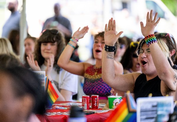 Three people cheer and hold their arms up while watching a drag performance. 