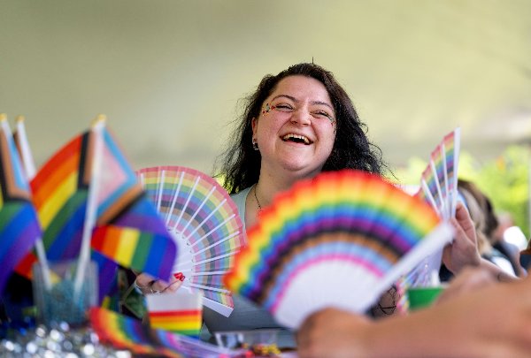 Kel Nemetz laughs framed by rainbow fans and pride flags. 