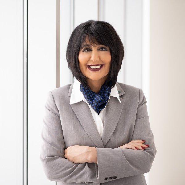 President Mantella standing in a hallway with arms crossed in a gray suit with blue scarf