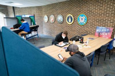 students sit and work at tables in the student veterans lounge in Kirkhof Center; military seals from all five branches are hung on the brick wall