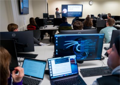 Faculty member teaches class in cybersecurity to room filled with students.