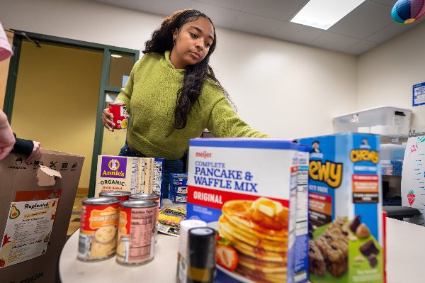 A young woman organizes a box of dry goods received by Replenish. 