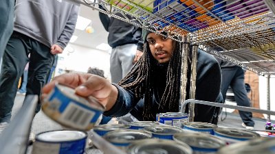 A young man places cans of tuna on a wire shelf at Replenish.