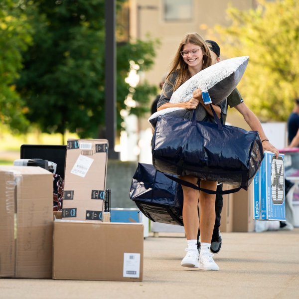 A student carries her belongings into a living center.