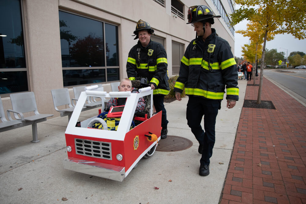 A child wearing a fire engine costume is escorted by Grand Rapids Fire Department firefighters.