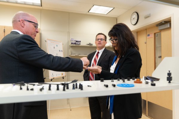 Brent Nowak, left, and President Philomena V. Mantella look at 3D pieces made at aMDI in this 2019 photo. John Hall, principle engineer and project manager, looks on.