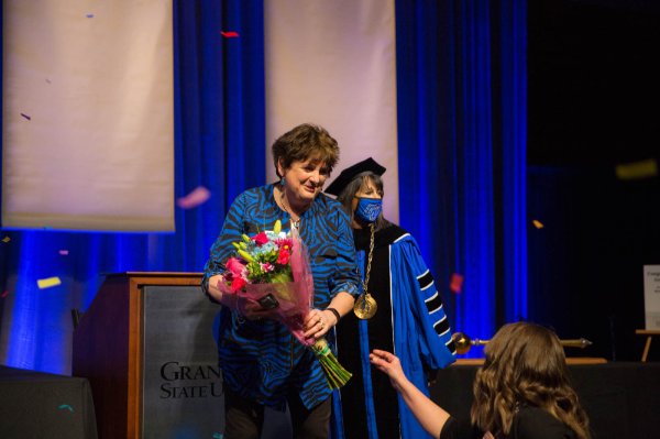 LeaAnn Tibbe accepts a bouquet of flowers while President Mantella is in the background in her academic regalia and a mask