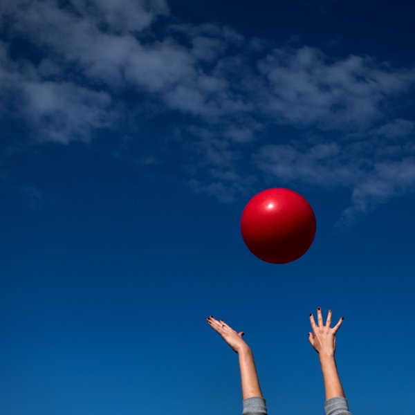 Hands reach high in the sky toward a large red ball in the air.