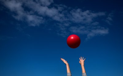 Hande reach high in the sky toward a large red ball in the air.