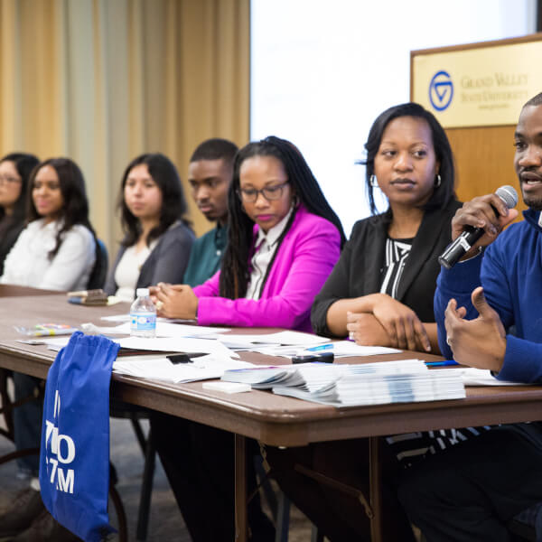 man speaking into microphone, people seated at table
