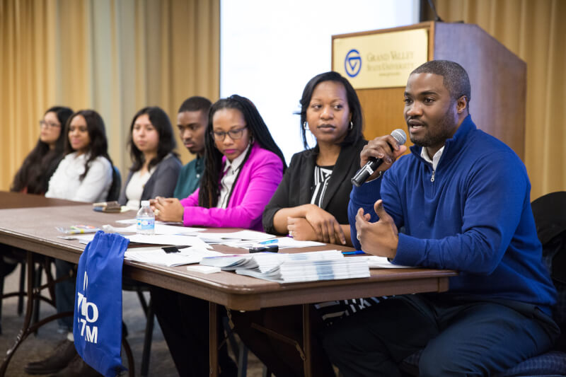 man speaking into microphone, people seated at table
