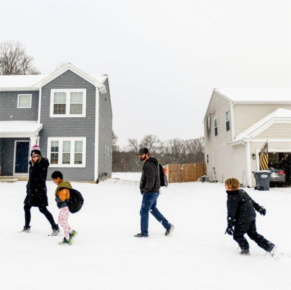 two parents and two young boys walk in the snow home from school in their neighborhood